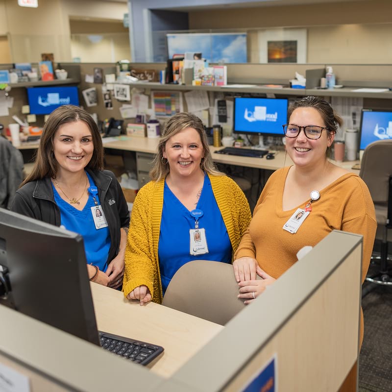 Three woman stand and smile at desks