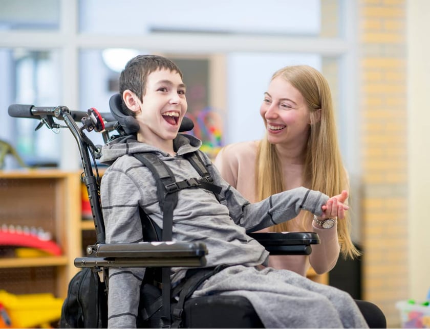 caregiver-laughs-with-young-boy-in-wheelchair