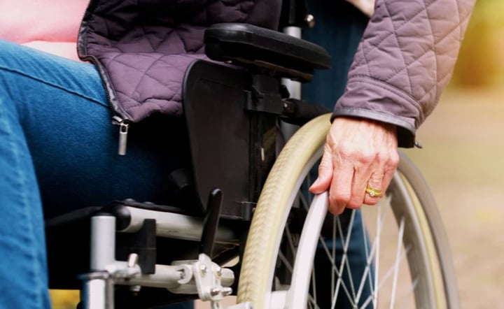 close-up-of-elderly-womans-hand-on-wheelchair-wheel-outdoors