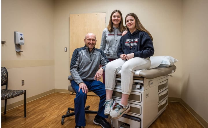 doctor-smiles-with-two-teen-patients-in-clinic-exam-room