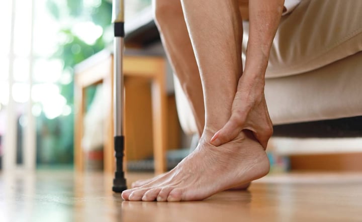 elderly-person-holding-painful-ankle-with-cane-nearby