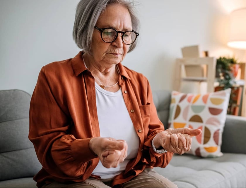 elderly-woman-examining-her-hand-while-sitting-on-couch-at-home
