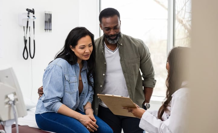The unrecognizable female doctor holds up the medical chart to show her female patient and her husband the test results they received.