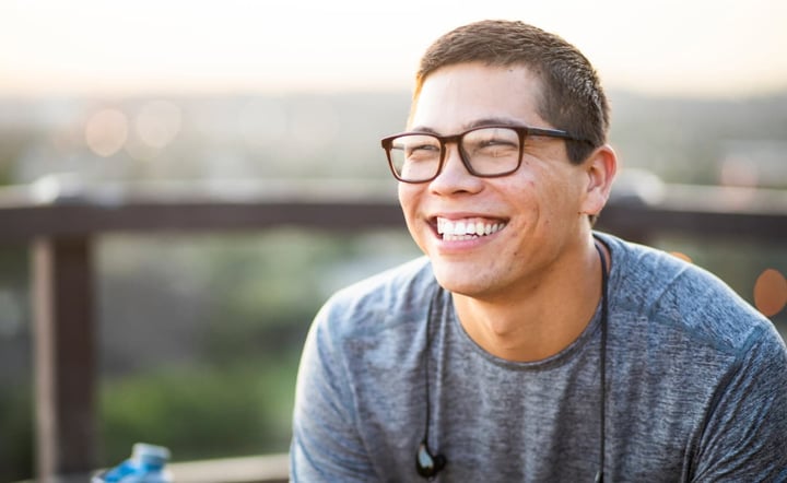 A portrait of an athletic young man outdoors wearing glasses smiling