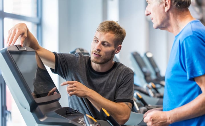 Trainer helping senior man exercising on treadmill