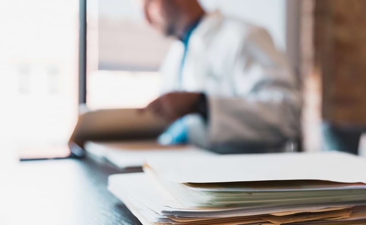 Close up of paper documents, blurred male doctor in background.