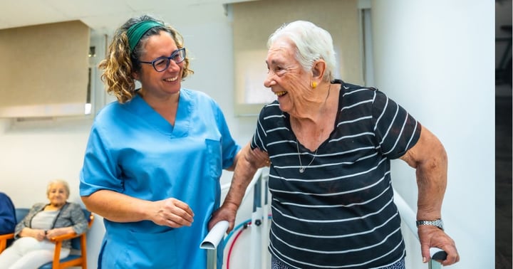 Senior patient doing physiotherapy at a geriatrics with help of a therapist walking on parallel bars