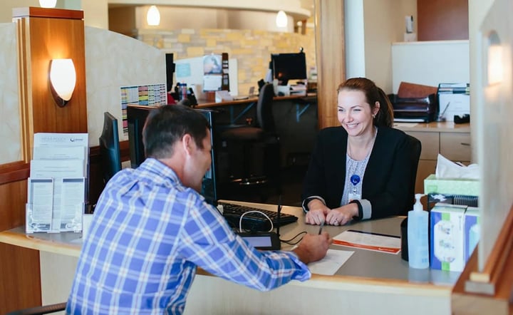A patient checks in at a medical office reception desk with a smiling staff member