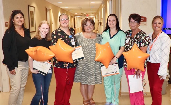 Group of people holding orange star balloons pose for a photo