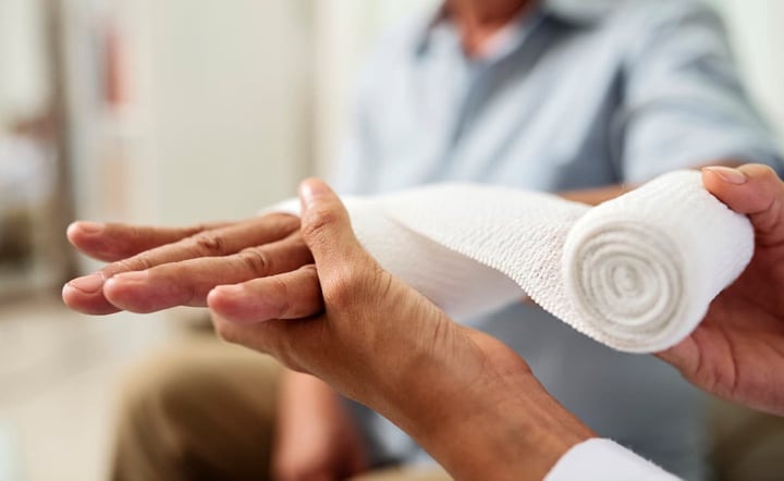 Close-up of nurse holding and bandaging hand of senior patient at hospital