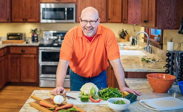 man-smiling-while-preparing-fresh-vegetables-in-home-kitchen