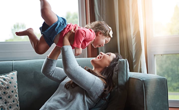 mother-laughing-and-lifting-toddler-in-the-air-playfully-at-home