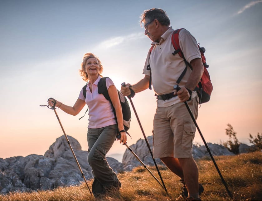 older-couple-hiking-with-trekking-poles-at-sunset