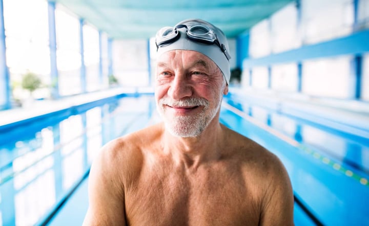 older-man-smiling-in-swim-cap-and-goggles-at-indoor-pool