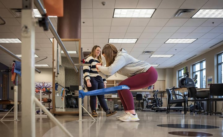 physical-therapist-assists-patient-with-balance-exercise-in-rehab-gym