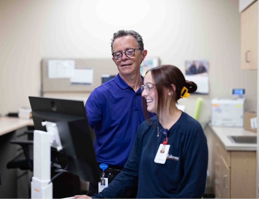 two-healthcare-staff-members-laughing-together-at-computer-in-clinic