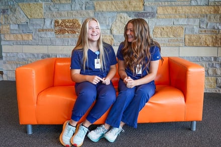 two_young_interns_sitting_on_orange_couch_laughing
