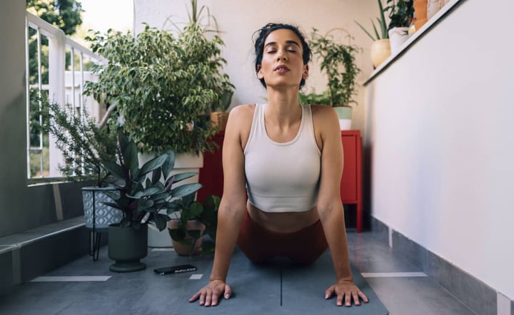 woman-practicing-yoga-cobra-pose-on-mat-surrounded-by-indoor-plants