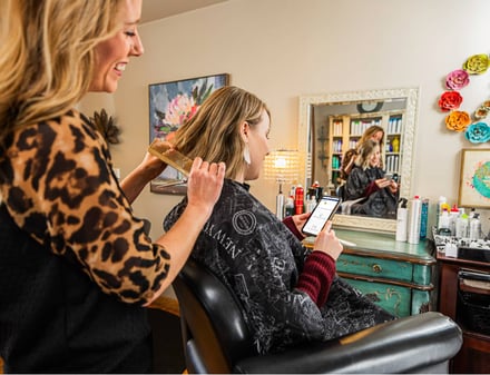 woman-schedules-medical-appointment-on-phone-while-getting-hair-done-at-salon