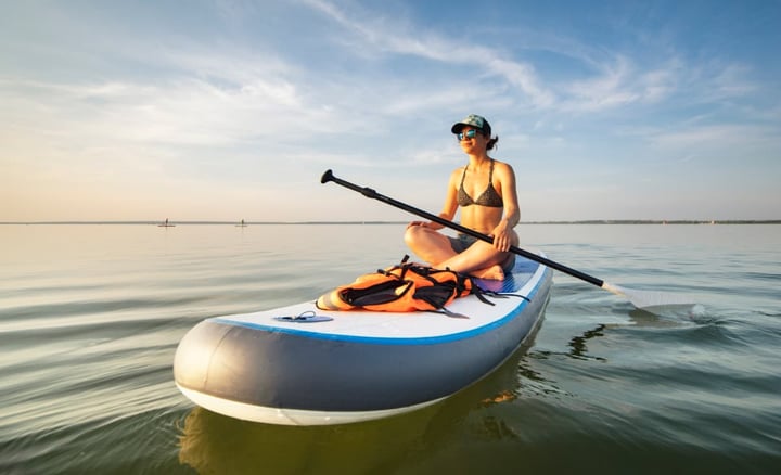 woman-sitting-on-paddleboard-on-calm-lake-at-sunset