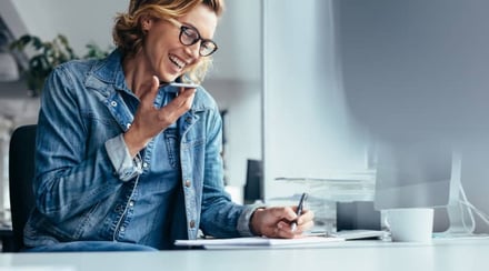 woman-talking-on-phone-while-taking-notes-at-desk
