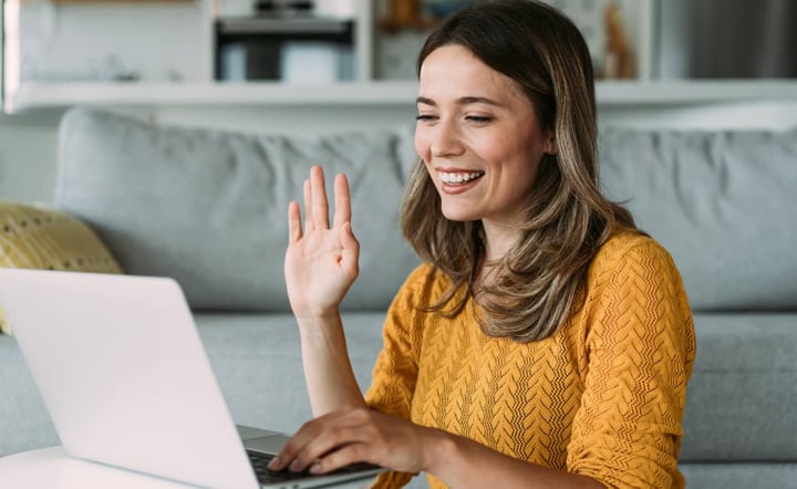 woman-waves-and-smiles-during-telehealth-video-appointment-at-home