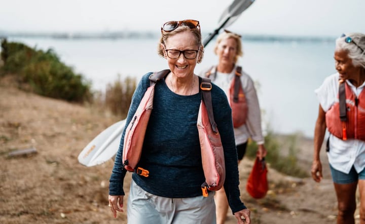 women-smiling-carrying-kayak-paddles-along-waterfront